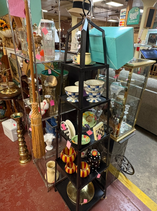 A tall black shelving unit filled with colorful bowls, plates, and decorative items, displayed among various antiques in a shop.